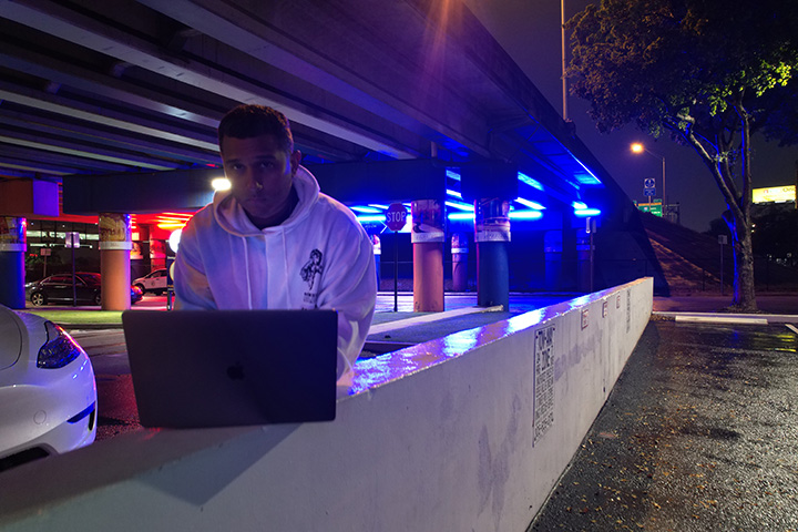 Image of Evan and neon lights under i95 in Miami's Art District with his Laptop